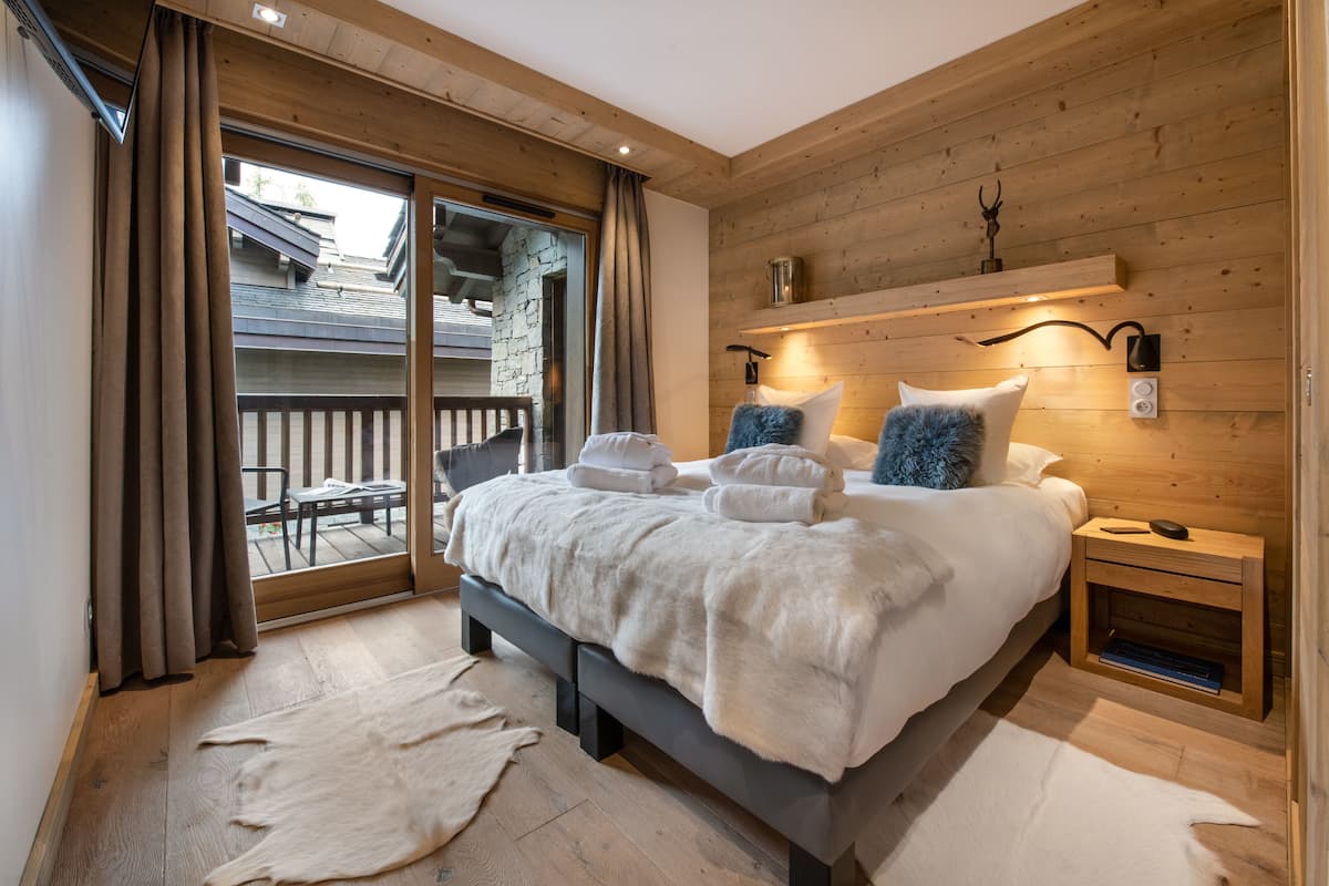 Ein Schlafzimmer mit einem großen Bett, Holzwänden, einem kleinen Nachttisch und Blick auf einen Balkon.