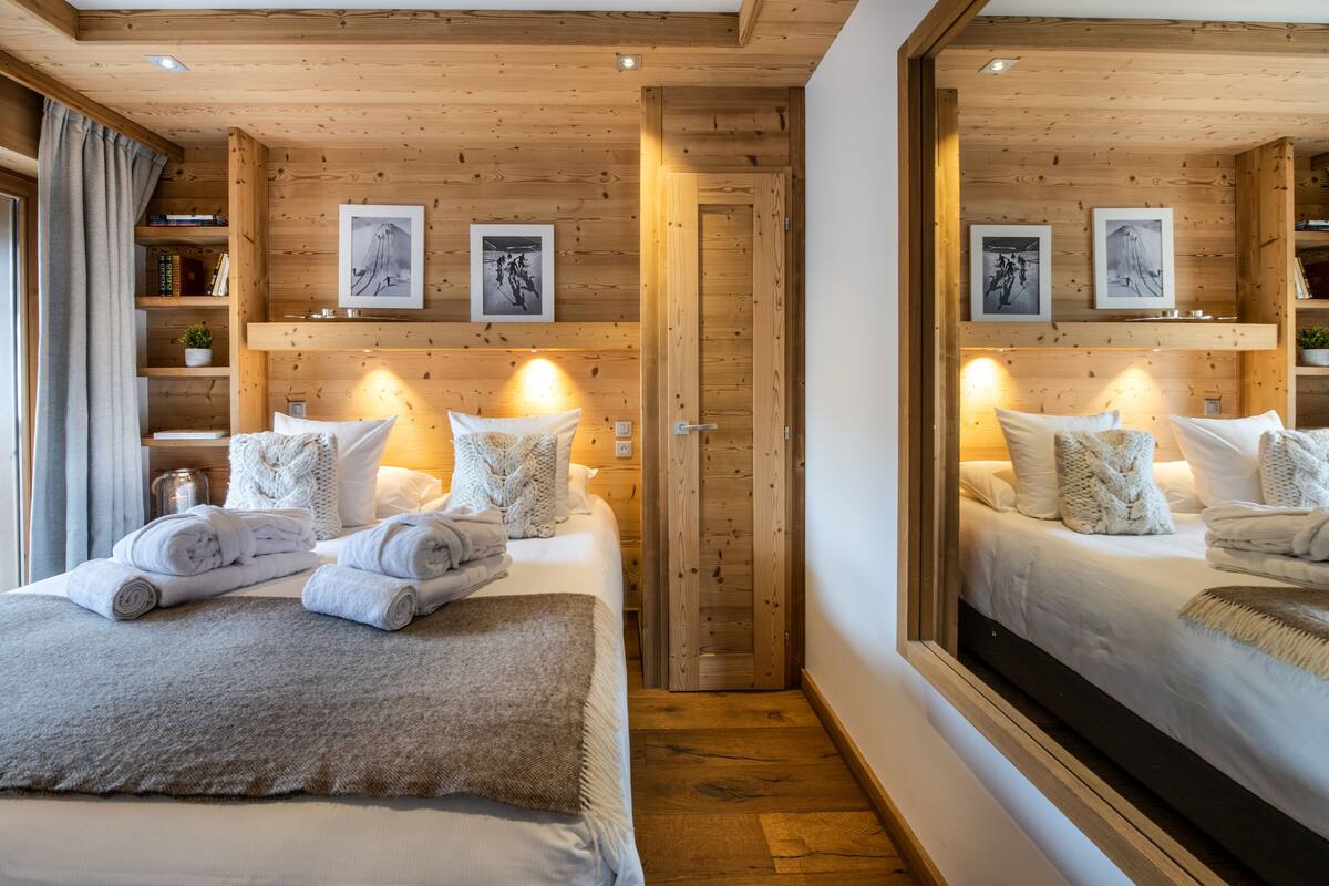 Un dormitorio acogedor con techo de madera, un espejo grande y una cama con toallas y almohadas ordenadas.