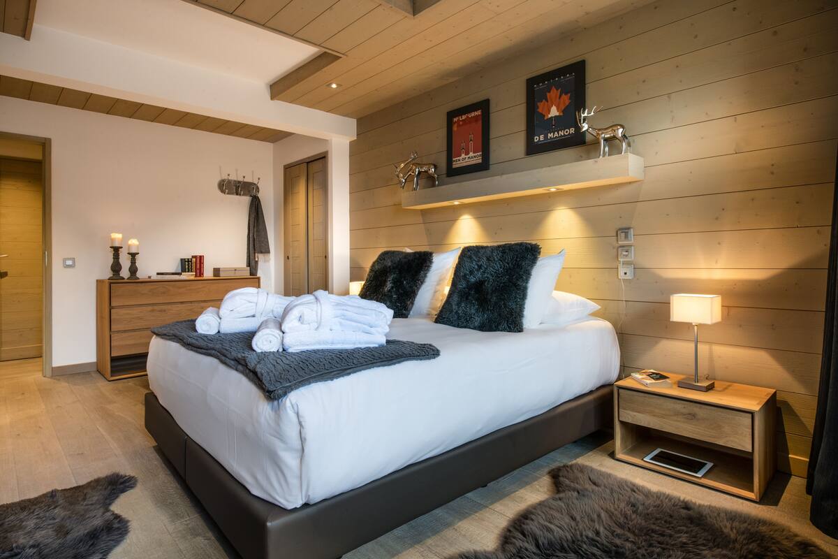 Un dormitorio moderno con una cama grande, mesitas de noche, una mesita auxiliar y un estante montado en la pared con objetos decorativos.