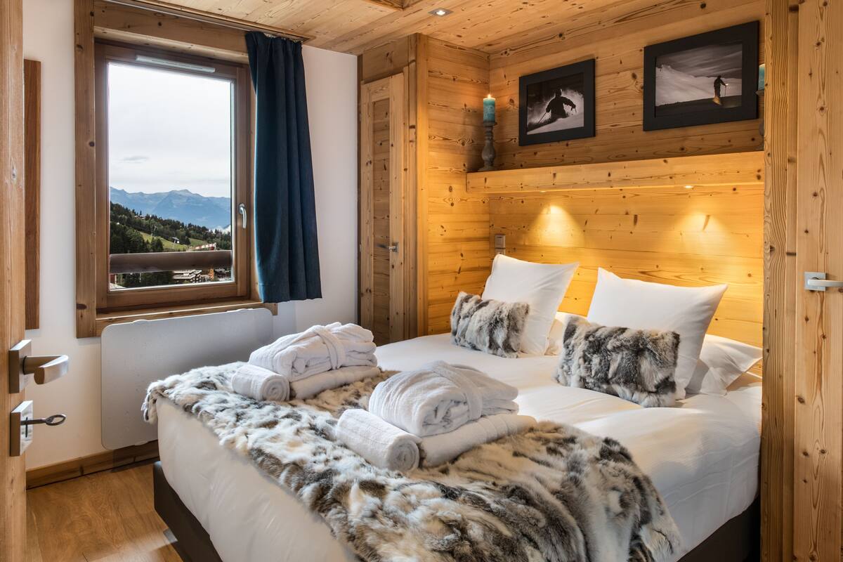 Una habitación con paneles de madera, una cama, toallas, un ventanal con vistas y cuadros enmarcados en la pared.