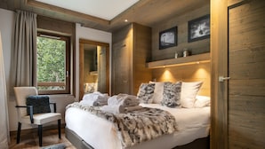 Een slaapkamer met een groot bed, een stoel, een vachttapijt, houten wanden en een raam met gordijnen.
