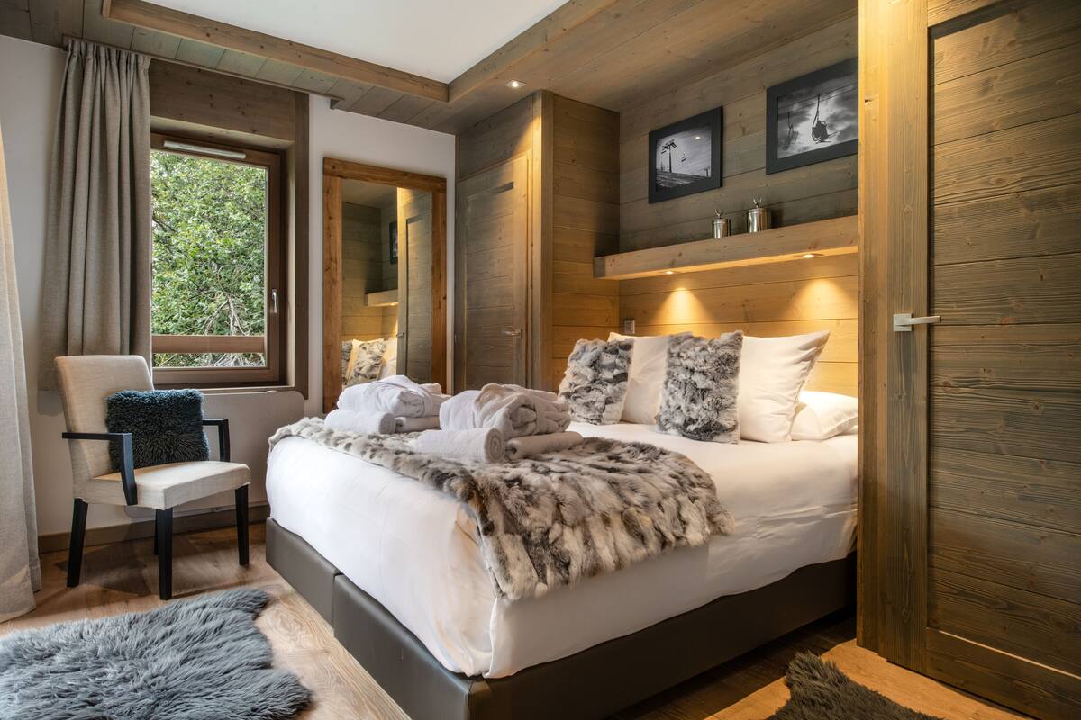 Un dormitorio con una cama grande, una silla, un alfombra de piel, paredes de madera y una ventana con cortinas.