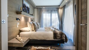 A modern bedroom with a wooden headboard, a large bed with multiple pillows, a bedside table with candles, and a fur throw.