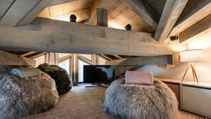 A cozy attic room with a television, two plush poufs, a lamp, and a woven rug.