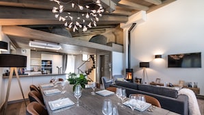 A dining area with a long wooden table set for six, a modern chandelier, and a cozy seating area with a fireplace.