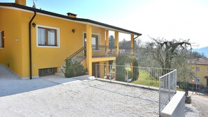 A yellow building with a balcony, a staircase, and a gravel driveway. - Orange Apartment In Marciaga di Costermano (Costermano)