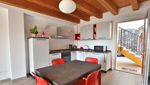 Eine moderne Küche mit weißen Schränken, einem Esstisch mit roten Stühlen und Blick auf eine Steintreppe, die zu einem Balkon führt.