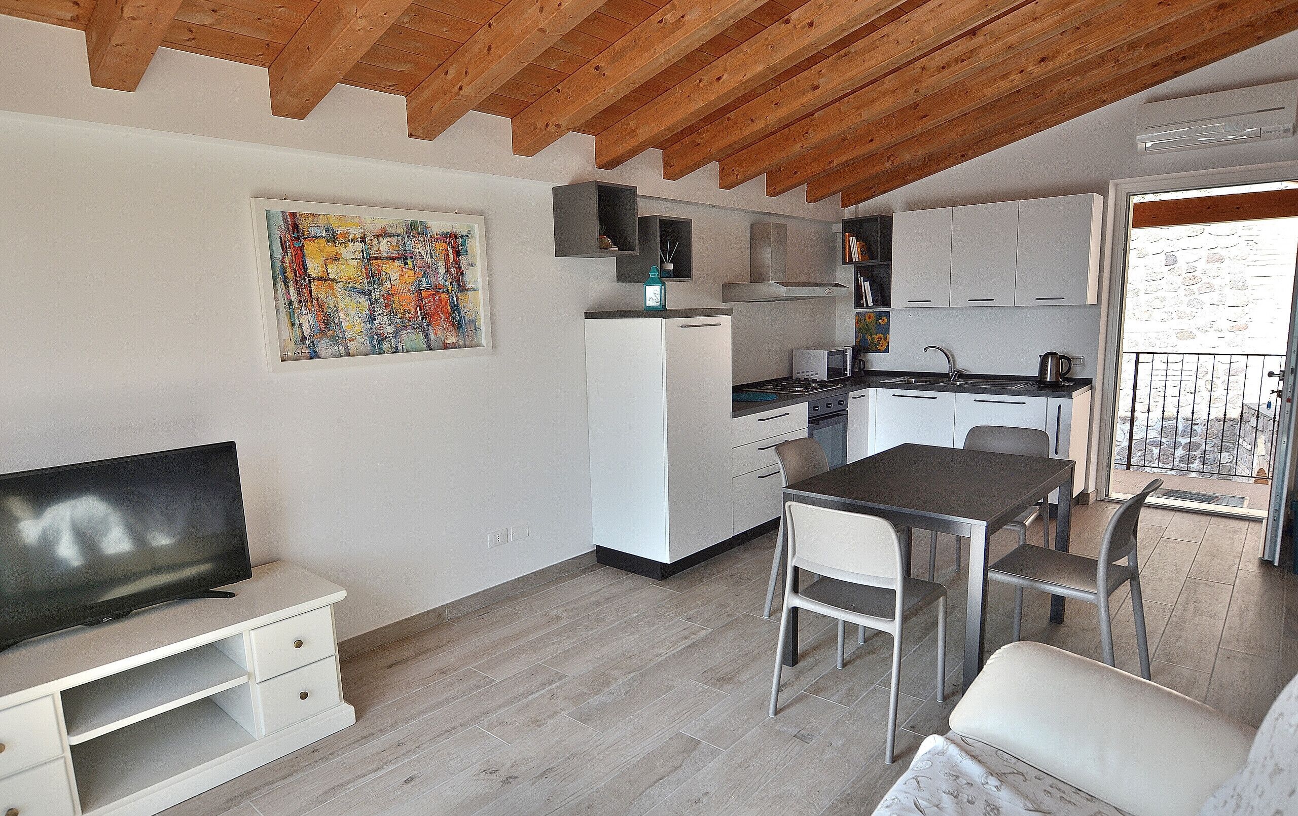 A compact kitchen with a dining area, a TV, and a balcony with a stone wall.