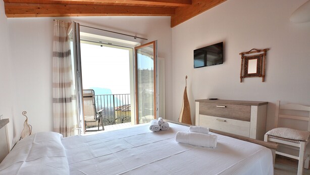 Une chambre avec un grand lit, une commode en bois, une chaise, un téléviseur et un balcon avec vue.