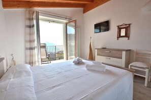 Ein Schlafzimmer mit einem großen Bett, einem hölzernen Schminktisch, einem Sessel, einem Fernseher und einem Balkon mit Blick.