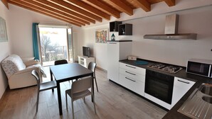 Une cuisine de taille réduite avec des poutres en bois, un coin repas avec une table et des chaises, un canapé et une vue dégagée sur l’extérieur grâce à une grande fenêtre.