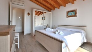Une chambre avec un plafond en bois, un lit recouvert de draps blancs, un bureau en bois et une chaise.