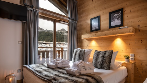A bedroom with a large bed, a wooden headboard, a window with curtains, and a view of mountains. - Aspen Lodge by Alpine resorts (Courchevel)
