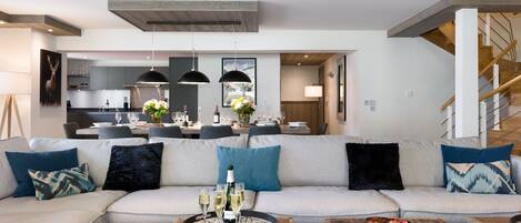 A modern living room with a sectional sofa, wooden coffee tables, and a dining area in the background.