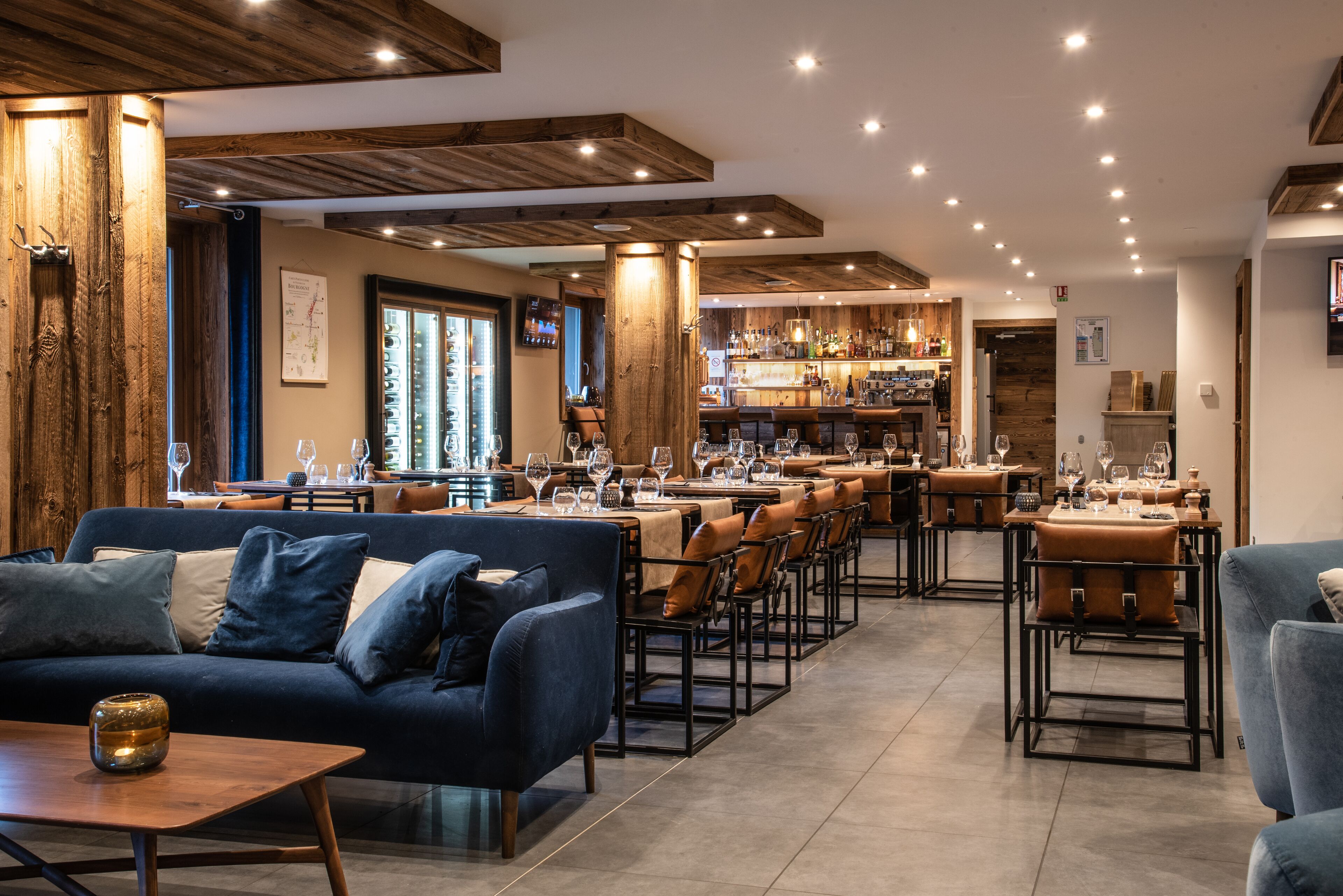 A modern restaurant with a bar area, wooden ceiling beams, and a cozy seating arrangement.