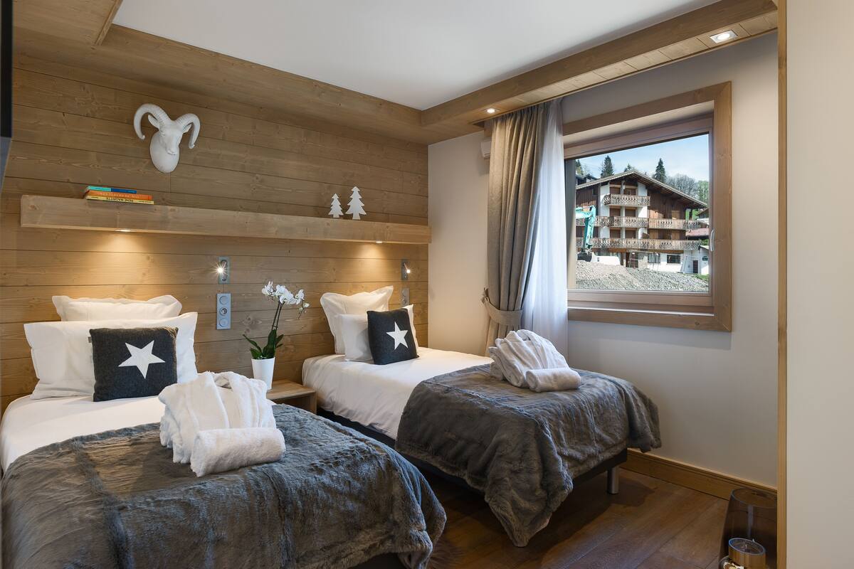 A hotel room with two beds, wooden ceiling, a mountain view, and a ski lift in the background.