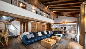 A spacious living area with a blue sofa, wooden coffee tables, and a staircase leading to an upper level.