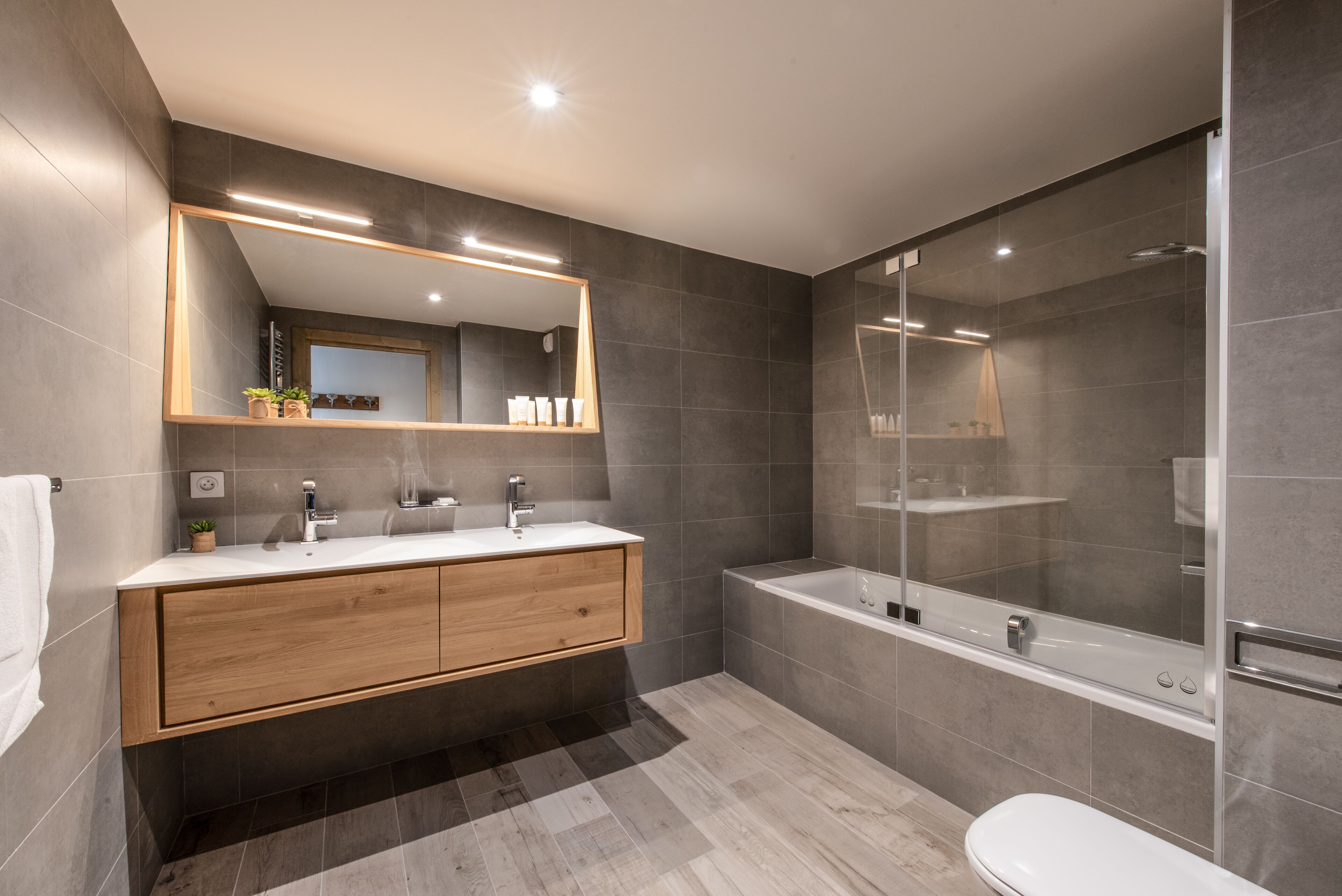 A modern bathroom with a wooden vanity, a large mirror, and a glass-enclosed shower.