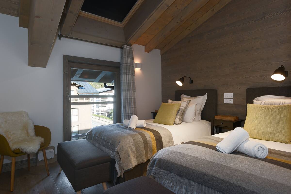 A cozy bedroom with two beds, a chair, and a window with curtains.