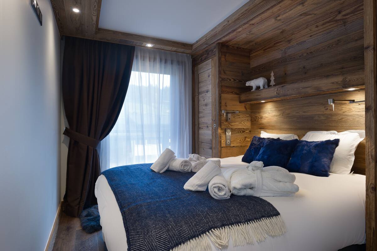 A hotel room with a wooden headboard, a bed with white and blue bedding, a blue throw blanket, and a set of towels.