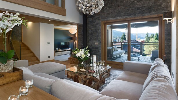 A modern living room with a glass coffee table, white sofas, and a large window with a mountain view.