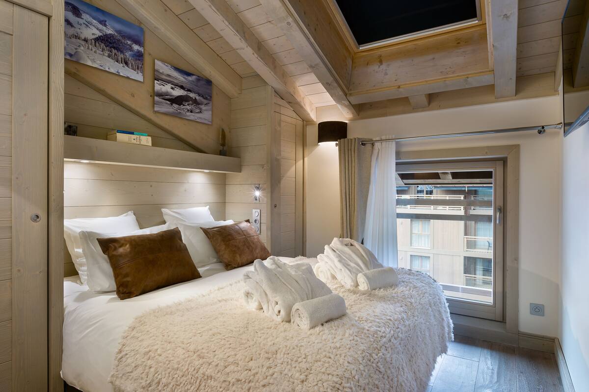A bedroom with a large bed, wooden headboard, and a window with a view of buildings.