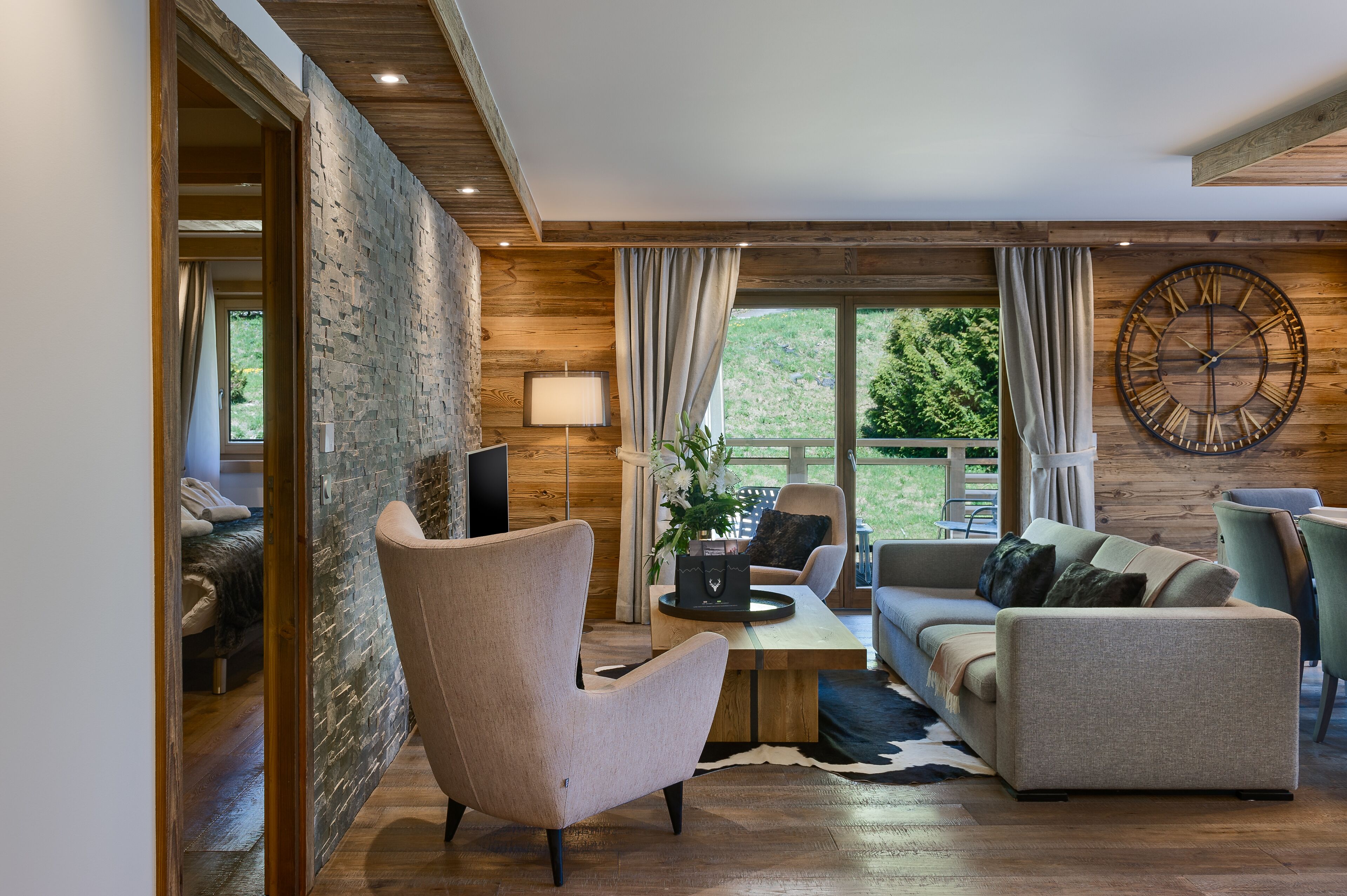 A modern living room with a stone wall, wooden ceiling, and large windows.