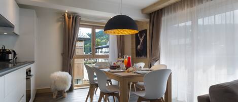 Un comedor con una mesa de madera, sillas blancas, un taburete mullido e una lámpara colgante negra.