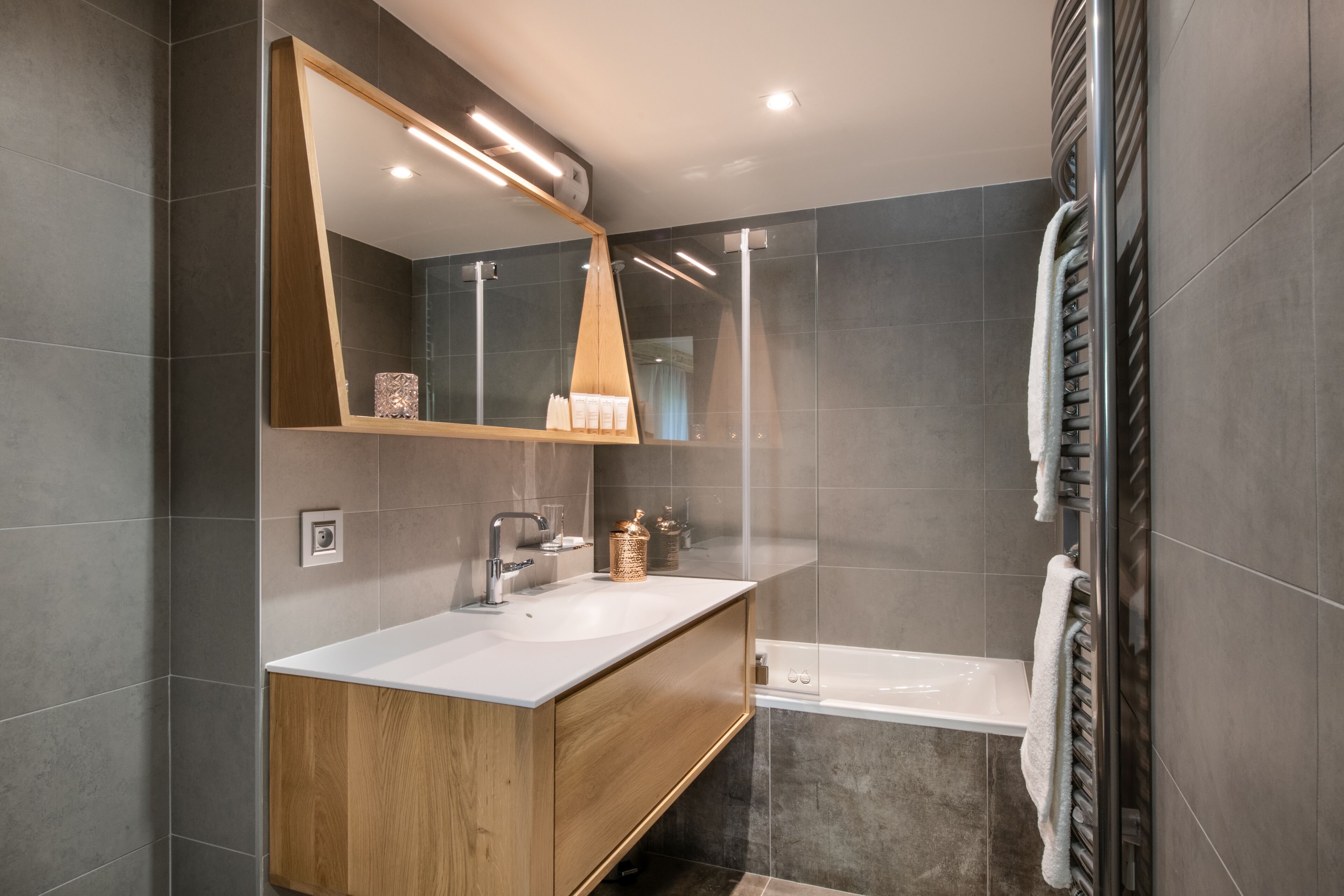 A modern bathroom with a wooden vanity, a large mirror, and a bathtub.