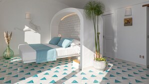 A modern bedroom with a white bed, blue pillows, and a geometric patterned floor.