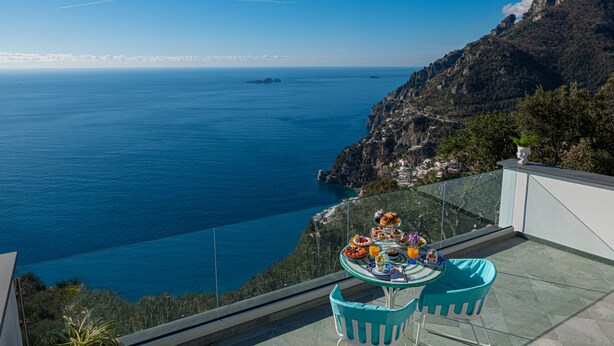 A terrace with a table set for breakfast overlooking a coastal view.