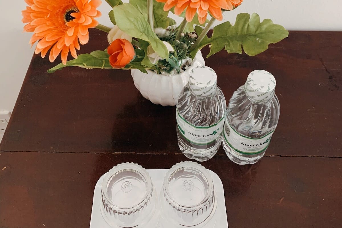 A table with a white vase containing orange flowers, two water bottles, and a tray with two empty glasses.