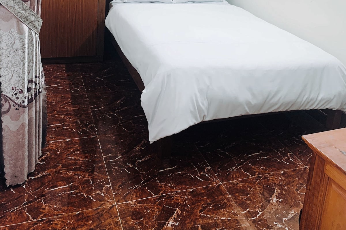A small, clean room with a bed, a wooden wardrobe, and a marble floor.