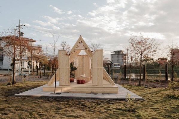 A wooden structure with a triangular roof, surrounded by grass and trees, with buildings in the background. - Star Deco Resort (Dongshan)