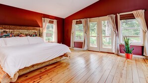 Un dormitorio con piso de madera, una cama grande, un ventilador de techo y una ventana con cortinas.