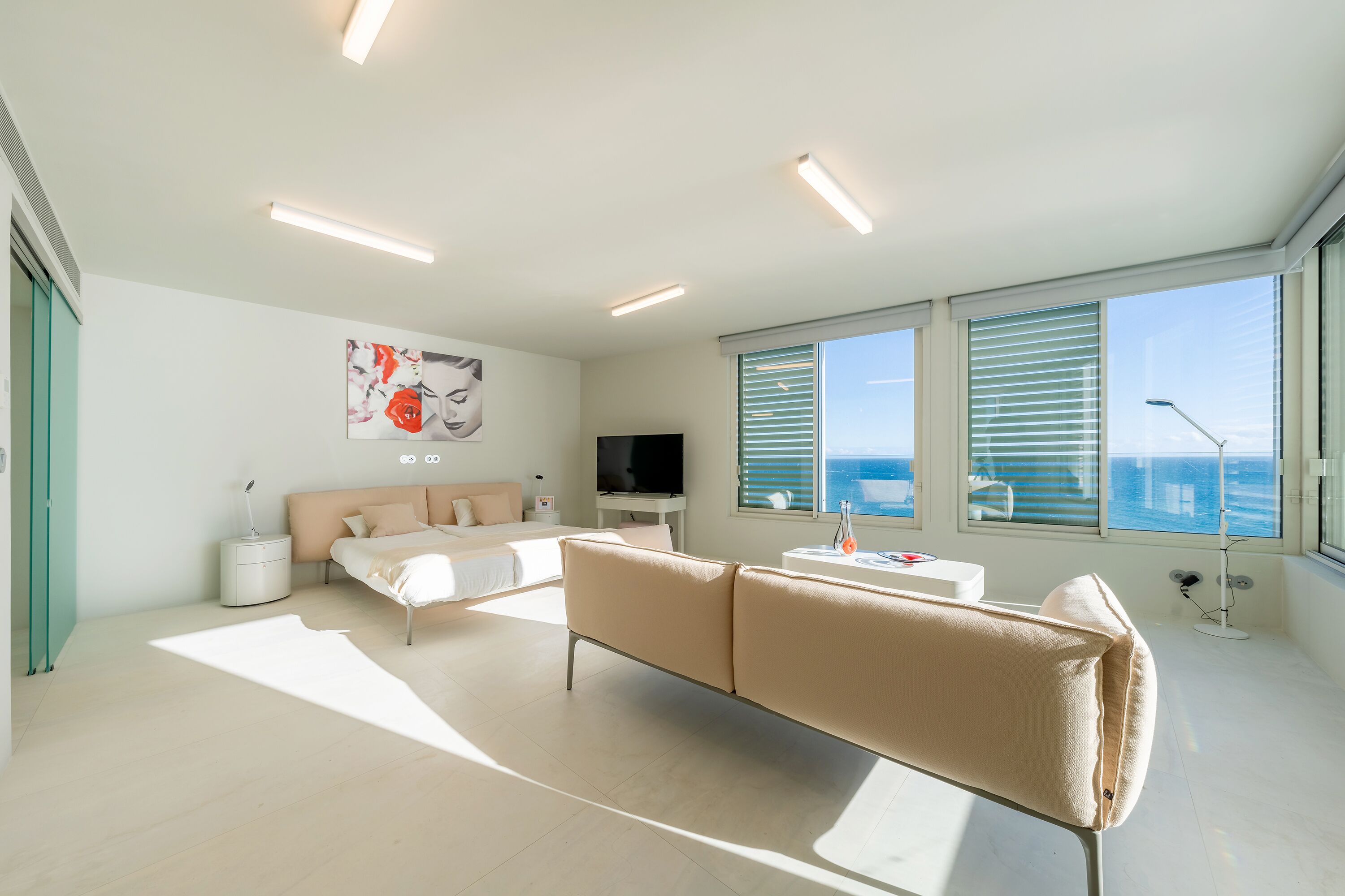 Ein modernes Wohnzimmer mit einer Couch, einem Fernseher und großen Fenstern mit Blick aufs Meer.