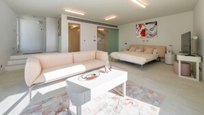 Egy modern szállodai szoba, amelyben van egy kanapé, egy ágy, egy kis asztal és egy televízió. Egy lépcső vezet a felső szintre.