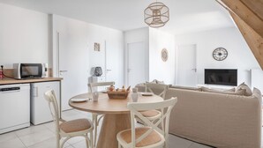 Une cuisine moderne équipée d’un four à micro-ondes, d’une machine à café et d’un réfrigérateur. On y trouve une table à manger avec des chaises, ainsi qu’un panier de pain. Un canapé et un téléviseur se trouvent dans l’espace salon.