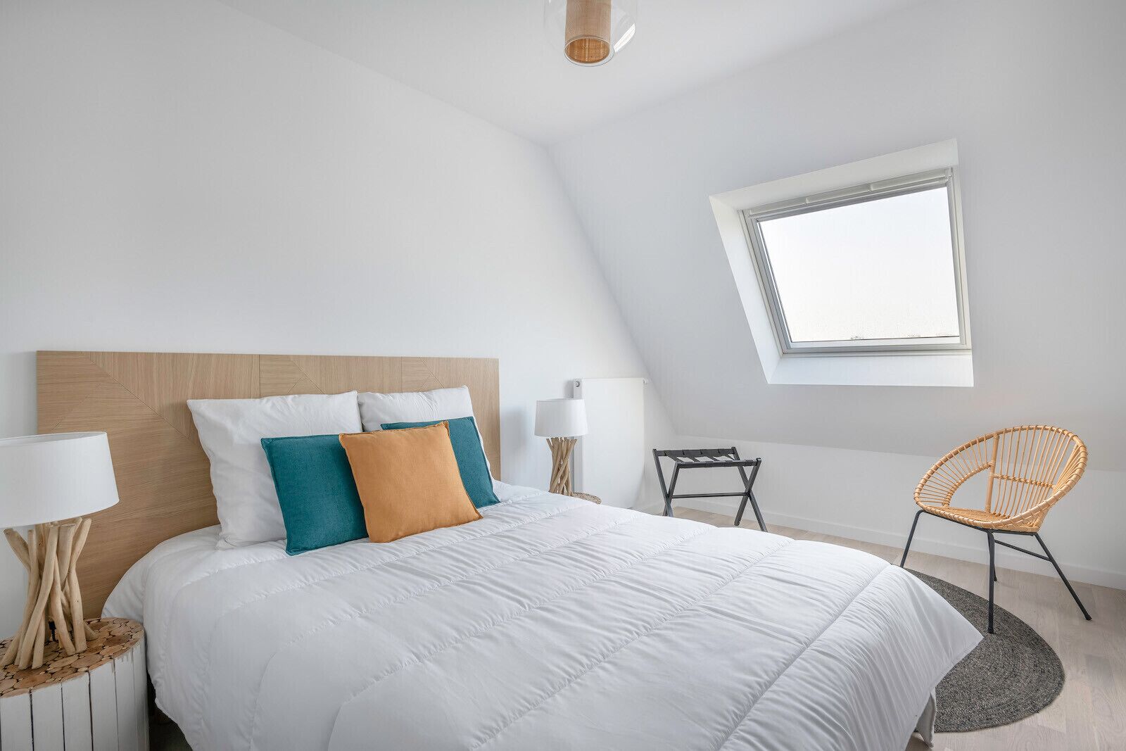 Una camera da letto moderna con un letto grande, un lucernario, una sedia in rattan e un tavolino.