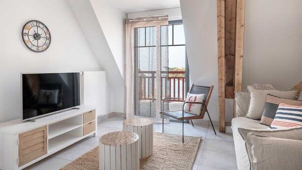Un salon moderne avec un téléviseur, des meubles blancs, une chaise en bois et un balcon avec vue.