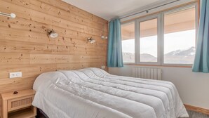 A bedroom with a wooden wall, a bed with white bedding, a nightstand, and a window with curtains. - Val Louron, 15-pers. apartment near slopes (Genos)