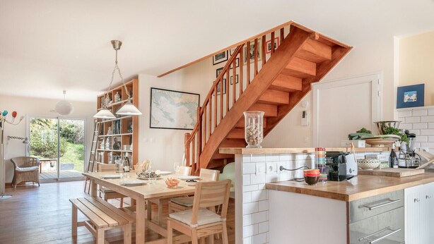 Una cocina moderna con suelo de madera, una escalera de madera y un comedor con mesa y sillas de madera.