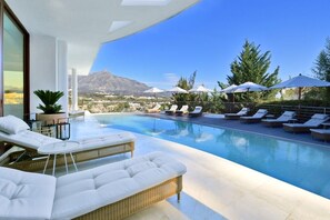 Un área de piscina exterior moderna con sillones de descanso y sombrillas, con vistas a un paisaje montañoso.