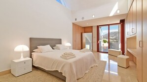 Un dormitorio moderno con una cama grande, lámparas de noche, vistas al exterior y un balcón.