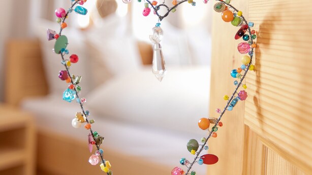 Une décoration en forme de cœur, ornée de perles colorées, suspendue à une poignée de porte.