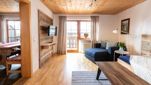Une pièce confortable avec un plancher en bois, un lit, un bureau avec une chaise, une télévision et une fenêtre avec des rideaux.