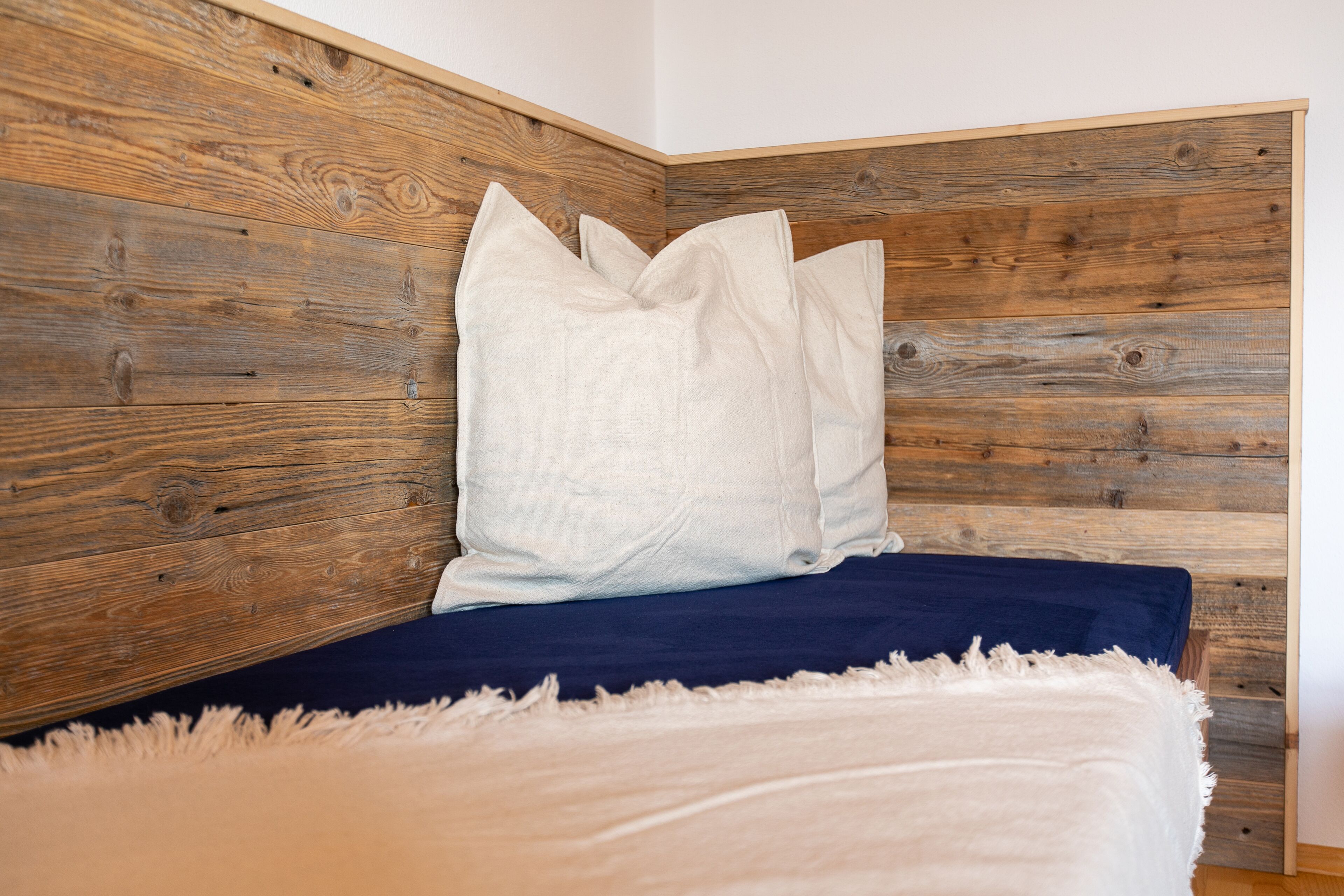 A bedroom with a wooden headboard, a white pillow, a blue bedspread, and a white throw blanket.