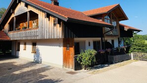 Une maison en bois à deux étages, avec un toit recouvert de tuiles rouges, de grandes fenêtres et un balcon.
