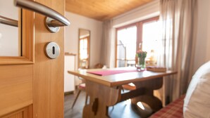 Une porte en bois, dotée d’une poignée et d’un trou de serrure, qui donne sur une pièce contenant une table en bois, une chaise et une fenêtre avec des rideaux.