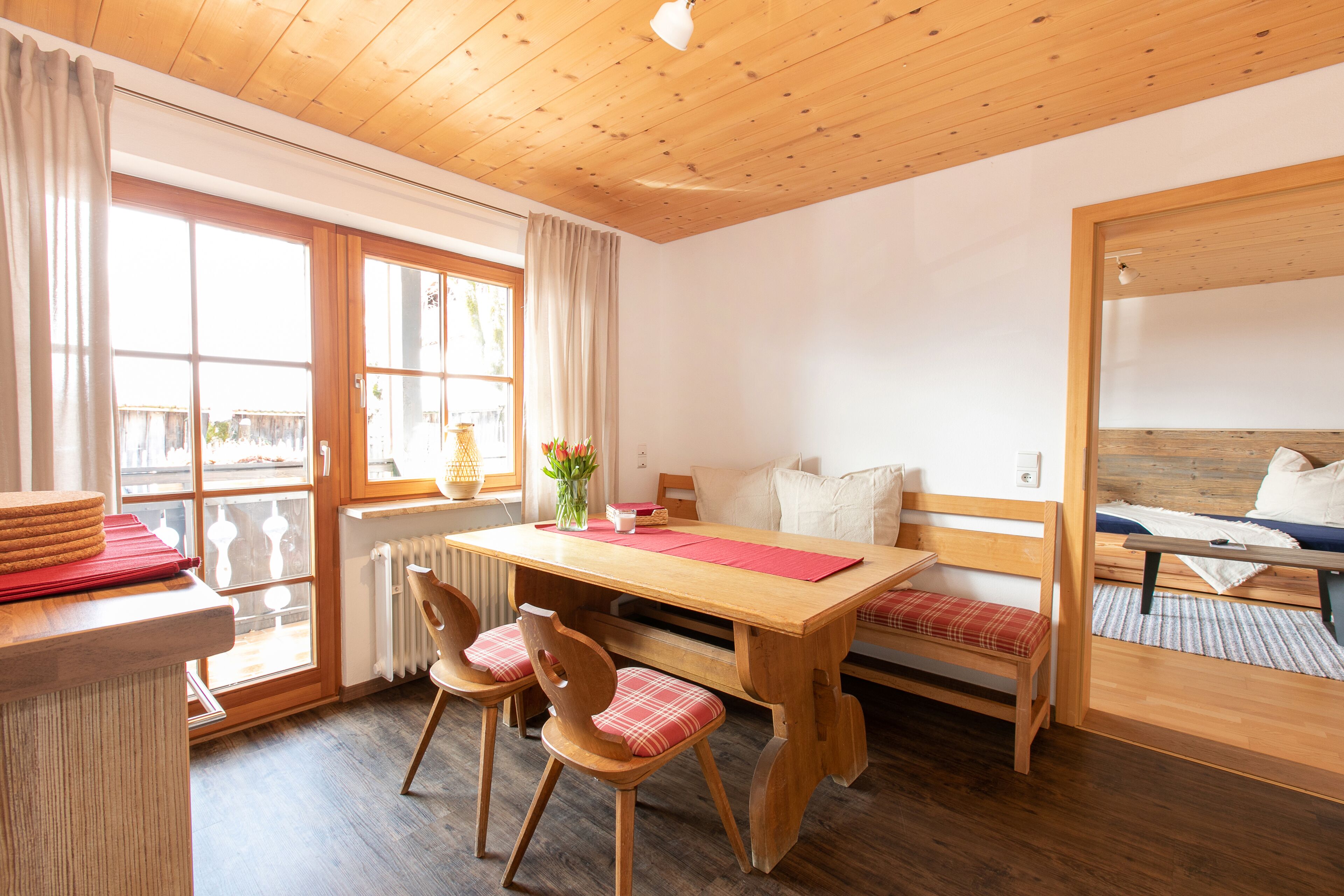A cozy room with a wooden dining table, two chairs, a bench, and a bed with a wooden headboard.